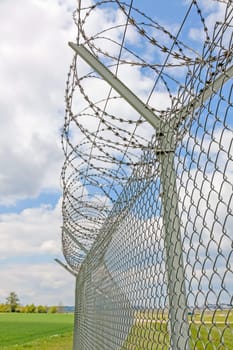 fence with barbed wire, green landscape and blue sky with clouds