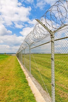 fence with barbed wire, green landscape and blue sky with clouds