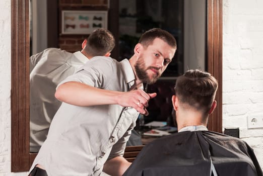 Young handsome barber making haircut of attractive bearded man in barbershop