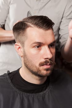 The hands of barber making haircut to attractive man in barbershop