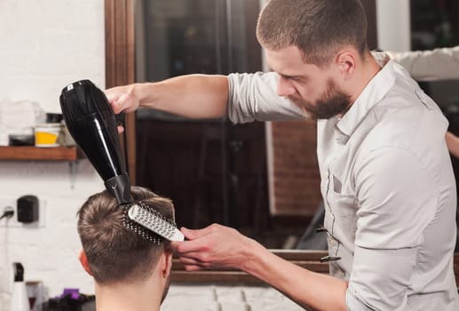 Young handsome barber making haircut of attractive bearded man in barbershop