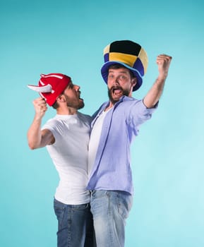 Two excited male friends celebrate watching sports on television over blue studio