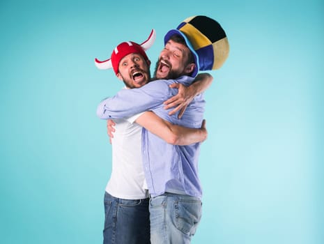 Two excited male friends celebrate watching sports on television over blue studio
