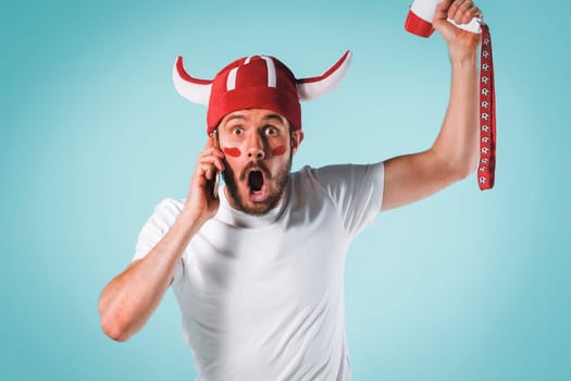 The football fan with megaphone over blue. The young man looking at camera with different emotions on face