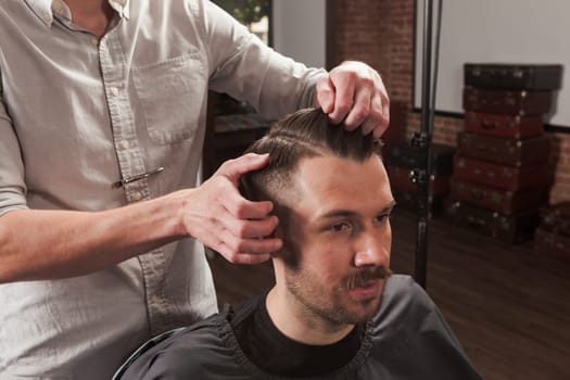 The hands of barber making haircut to attractive man in barbershop