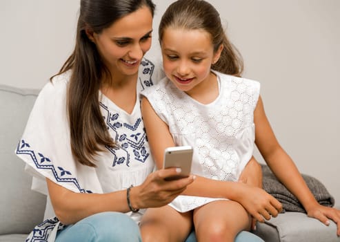 Beautiful Mom and Daughter at home, showing something on the phone