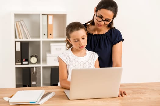 Mom teaching Daughter working with a a laptop at home