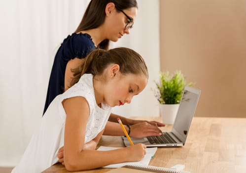 Mom teaching Daughter working with a a laptop at home