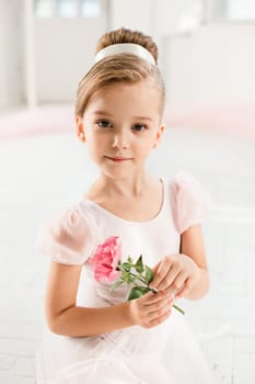 The little balerina in white tutu in class at the ballet school sitanding on the wooden floor with flowers