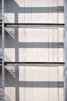 A steel railing with an external staircase casts symmetrical shadows on a concrete wall.