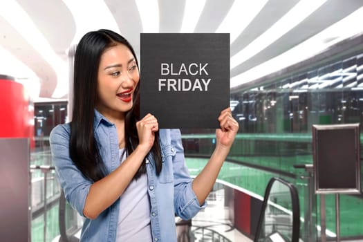 Young asian woman holding sign board with Black Friday text on the mall