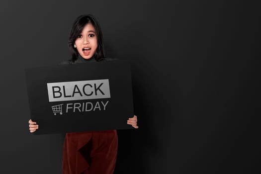 Excited asian woman holding banner with Black Friday announcement over black background