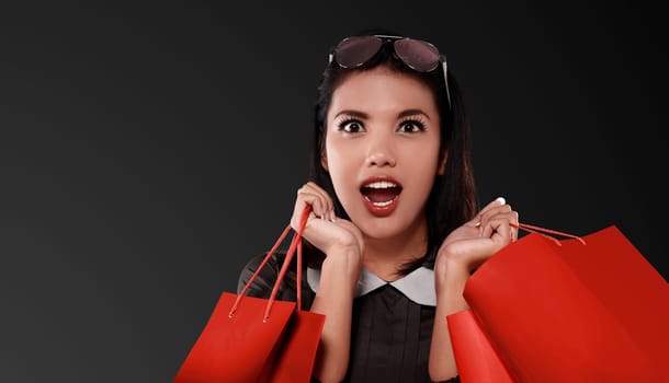 Happy asian woman with red shopping bag celebrating Black Friday over black background
