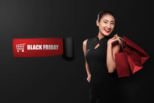 Happy asian woman holding paperbag with Black Friday text on ripped paper