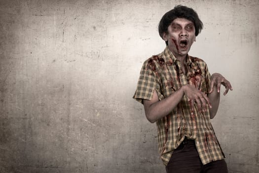 Spooky and bloody asian zombie man in a clothes standing against dirty background