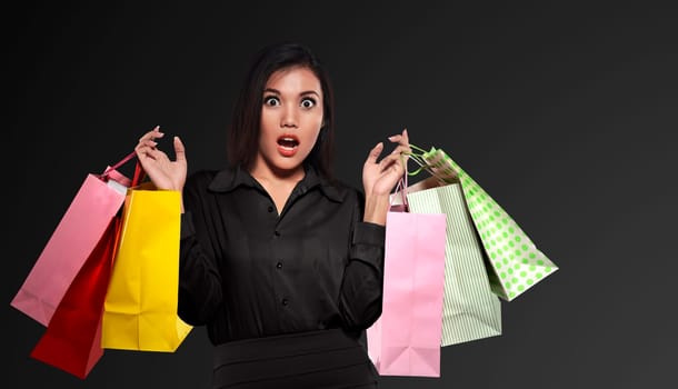 Excited asian woman holding colorful paper bag celebrating Black Friday over black background