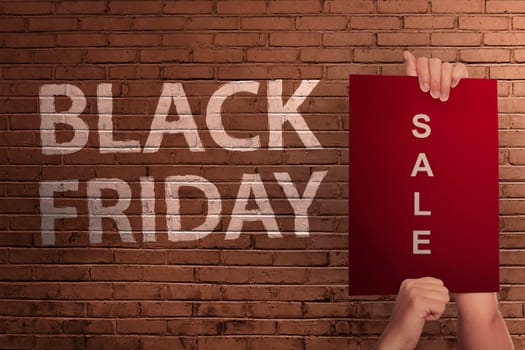 Black Friday text with hand holding sale banner against wall background