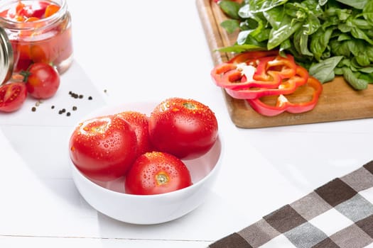 Canned tomatoes and fresh tomatos and other cut vegetables on white background