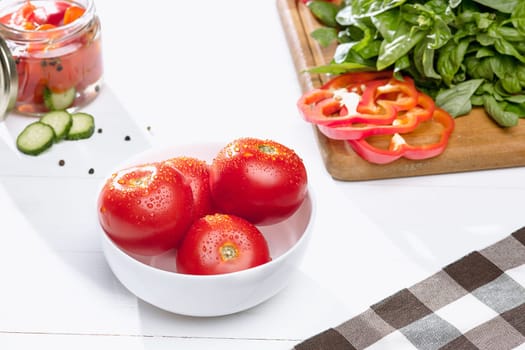 Canned tomatoes and fresh tomatos and other cut vegetables on white background