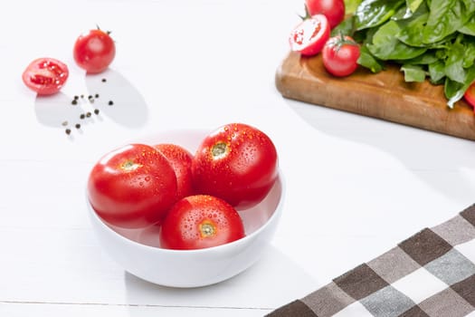 The fresh tomatos and other cut vegetables on white wooden table background