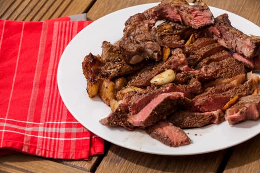 Sliced medium pink cooked beef on a plate with napkin on a wood base