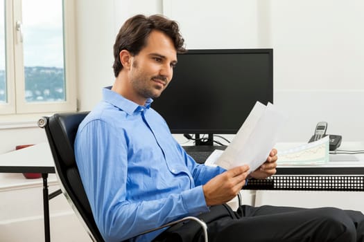 Young businessman sits with documents at a grater table in the office and informs himself