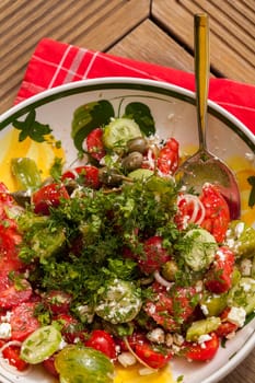 Bowl of marinated Greek salad with tomato cheese and olives on a wood edible