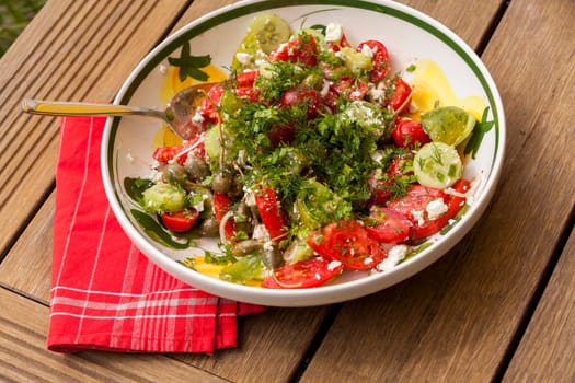 Bowl of marinated Greek salad with tomato cheese and olives on a wood edible