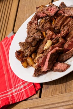 Sliced medium pink cooked beef on a plate with napkin on a wood base