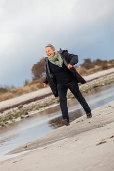 happy active older woman pensioner senior in the open at the sea in autumn