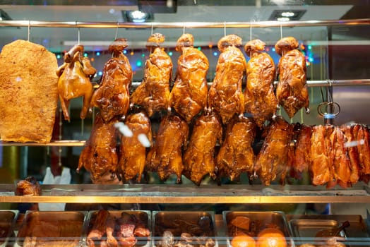 Detail of Chinese restaurant with traditional crispy ducks hanging on foggy display window in London's Chinatown at night.