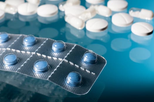 Blue pills in strip with white medicine pills and capsules in blue background