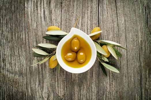 Olive oil with olive leaves on wooden background