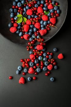 Mix of fresh berries in a bowl on black background