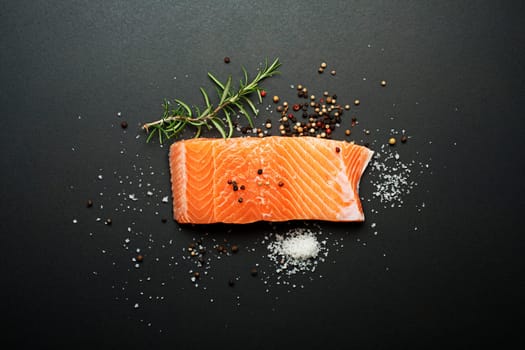 Raw salmon fillet and ingredients for cooking on a dark background
