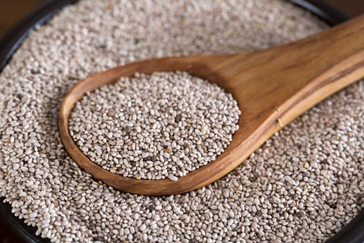 Healthy white chia seeds in bowl with wooden spoon.
