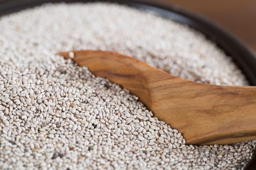 Healthy white chia seeds in bowl with wooden spoon.