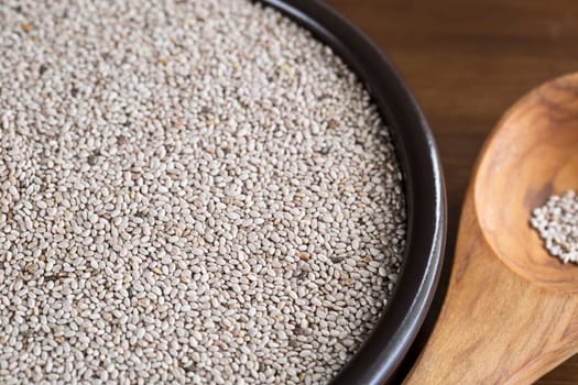 Healthy white chia seeds in bowl with wooden spoon.