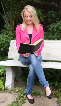 Beautiful woman reading a book outdoors while sitting on a concrete bench