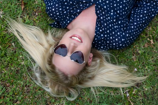 Lovely young lady relaxing on the grass and wearing heart shaped sunglasses