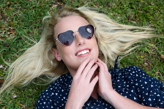 Lovely young lady relaxing on the grass and wearing heart shaped sunglasses