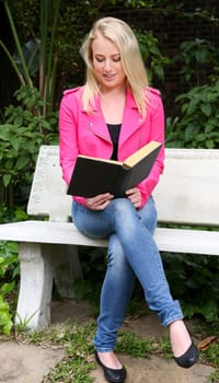 Beautiful woman reading a book outdoors while sitting on a concrete bench