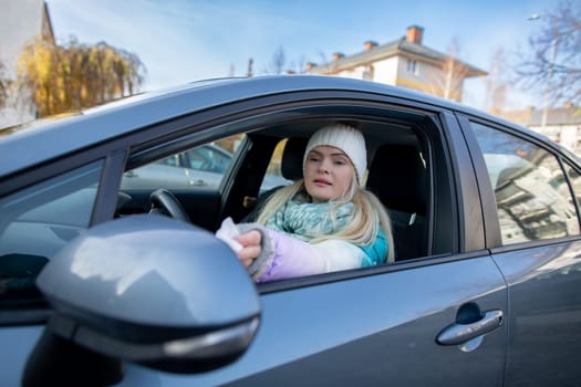 A young woman wearing a stylish winter hat and warm scarf is sitting comfortably in a car, showing off a chilly day