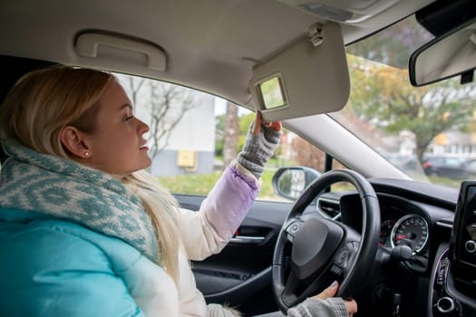 A woman in a cozy jacket adjusting the sun visor while driving, showcasing modern automotive interior.