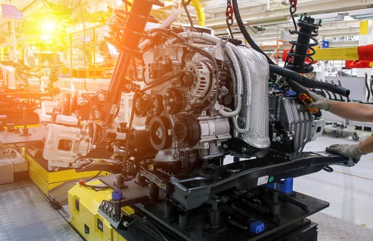 Workers are assembling an automotive engine on a conveyor system in a well-lit factory, focusing on precision and efficiency.
