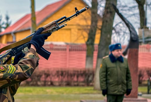 Soldiers perform a formal salute at a memorial, showcasing discipline and respect in a public ceremony in a village setting.