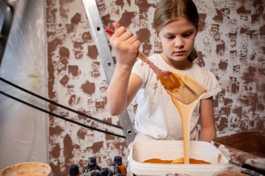 A young girl is actively and creatively mixing orange paint, beautifully capturing the essence of childhood artistry