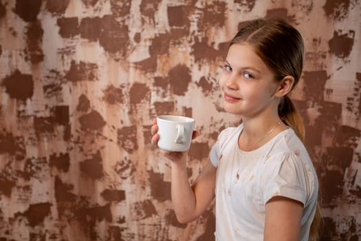 A cheerful young girl beams joyfully while holding a cup against a beautifully textured brown backdrop