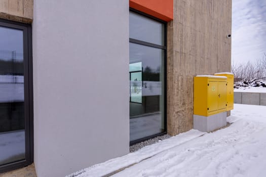 A contemporary architectural building is showcased with snowcovered surroundings and a bright yellow utility box