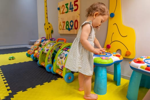 Toddler exploring a colorful activity table in an engaging playroom, discovering shapes and sounds. Concept of early learning and fostering creativity through interactive play